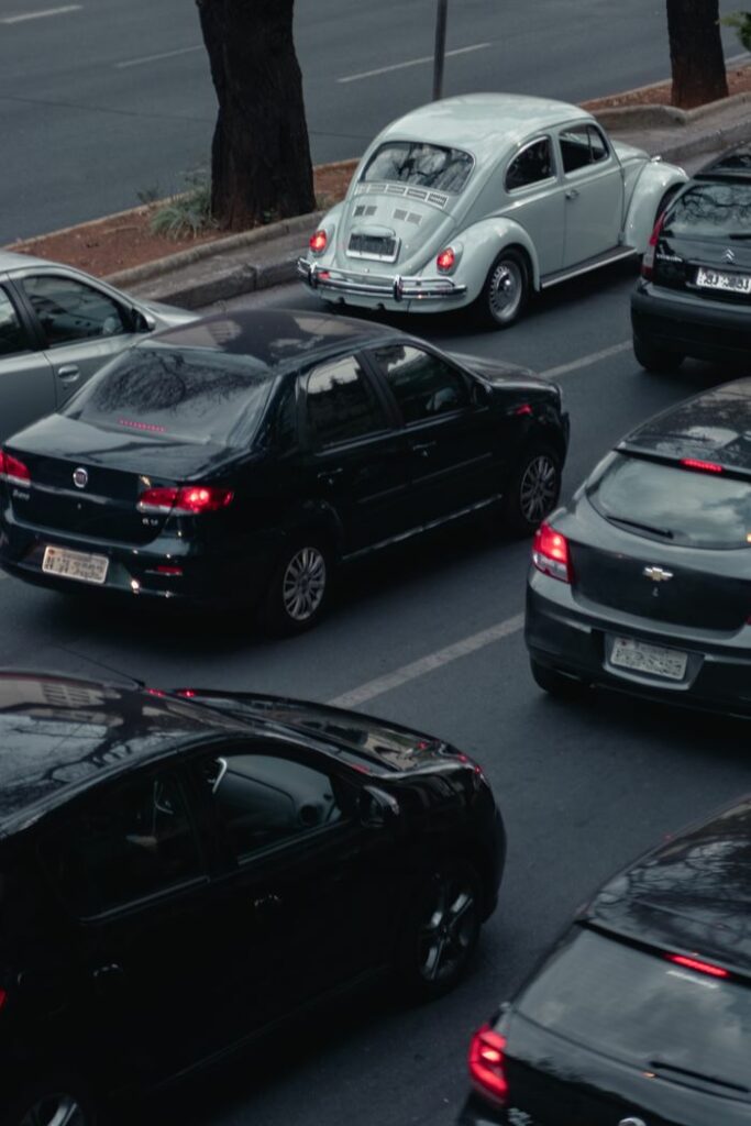 A vintage white beetle amidst modern cars on a busy city road.